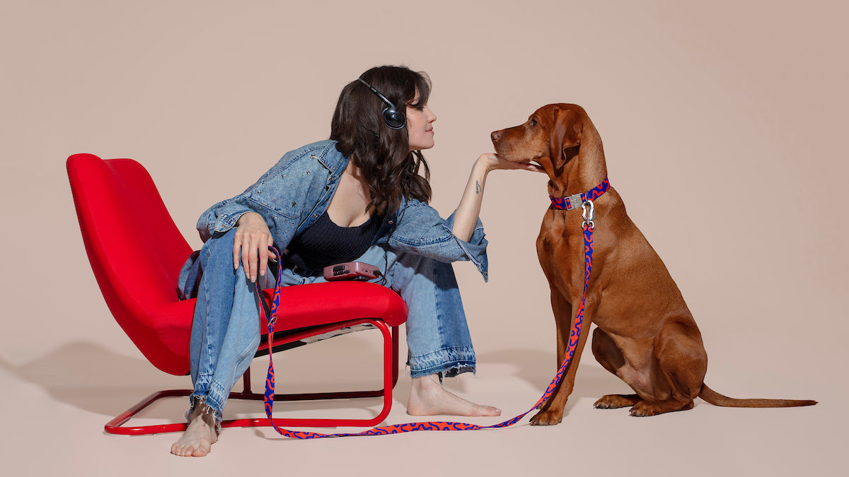 Woman sitting on a red chair with a dog on a beige background.