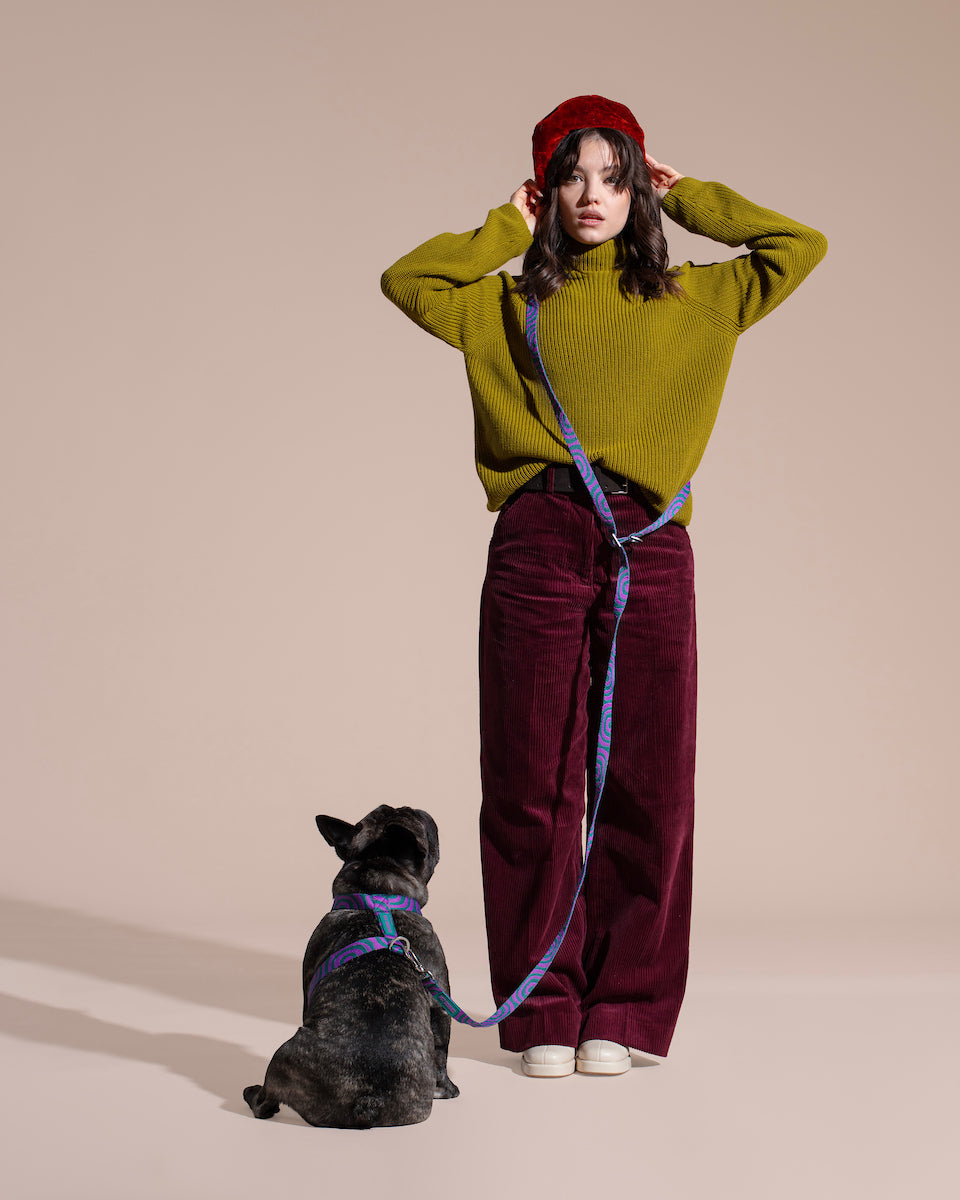 Woman in green sweater and red beanie with a dog on a LOLA GROOVE HANDS-FREE LEASH against a beige background.