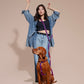 Woman in denim outfit with a dog on a leash and harness against a beige background.