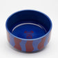 Front view of Hot Doggies Fusion ceramic bowl with vibrant blue and red striped design, durable and dishwasher safe.