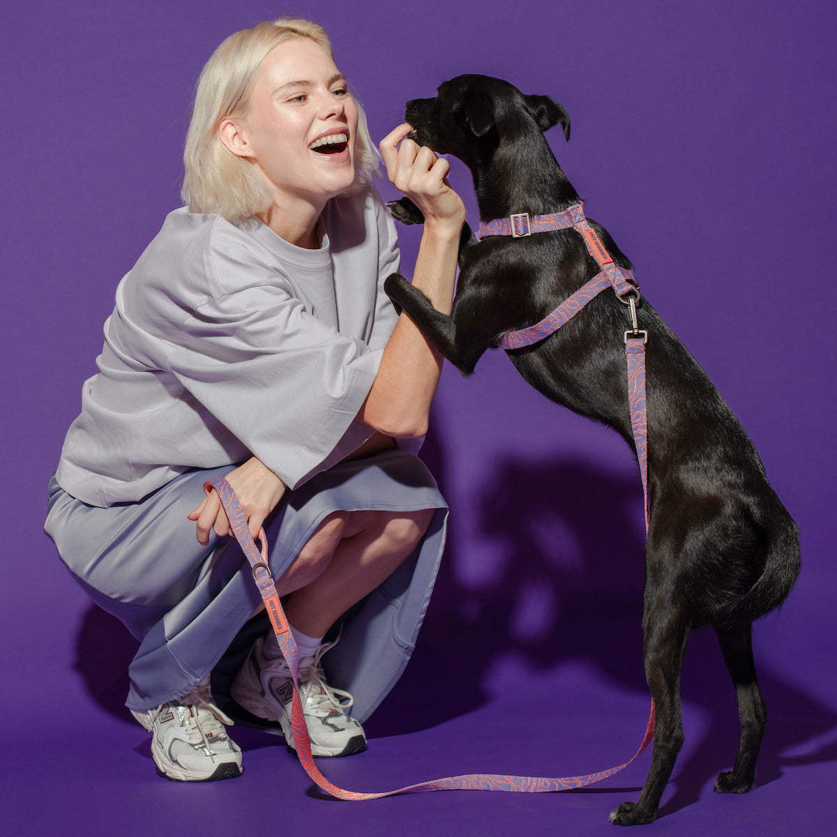 Female model giving a treat to her dog, both wearing the Lily Coral Doodle Pattern Harness, showcasing comfort and style.