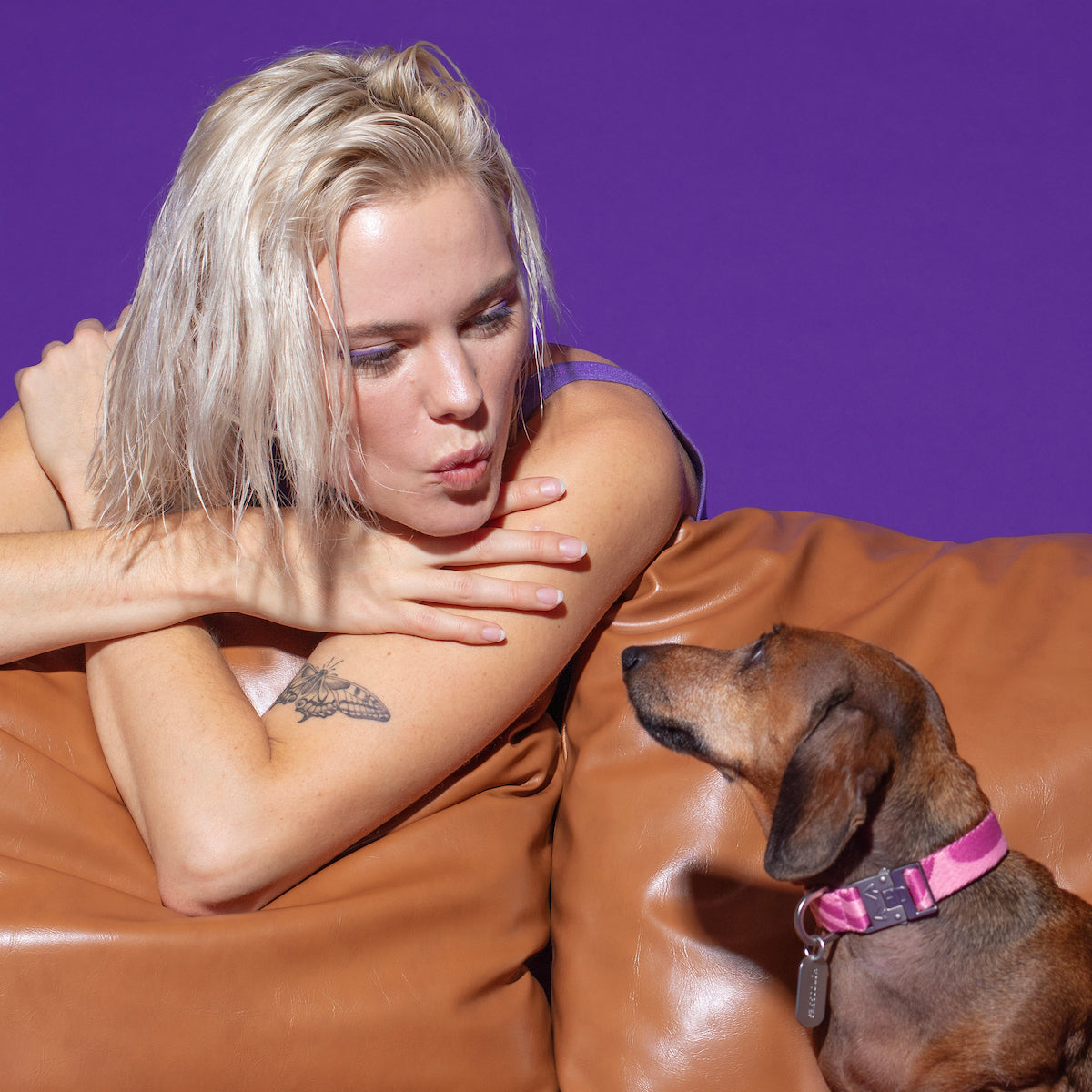 Dog wearing the Roxy Pink Collar on a sofa, accompanied by a model, featuring a vibrant pink wave design and durable buckle for a stylish and comfortable fit.
